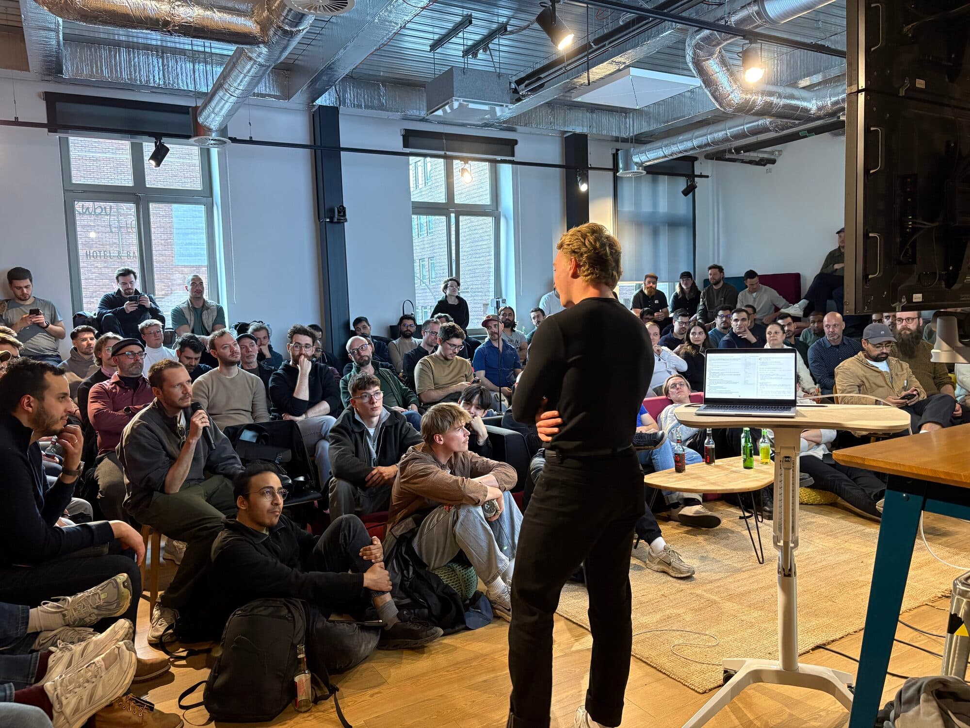 A host opening a session for a full room of members on a wooden floor at an AI BEAVERS event