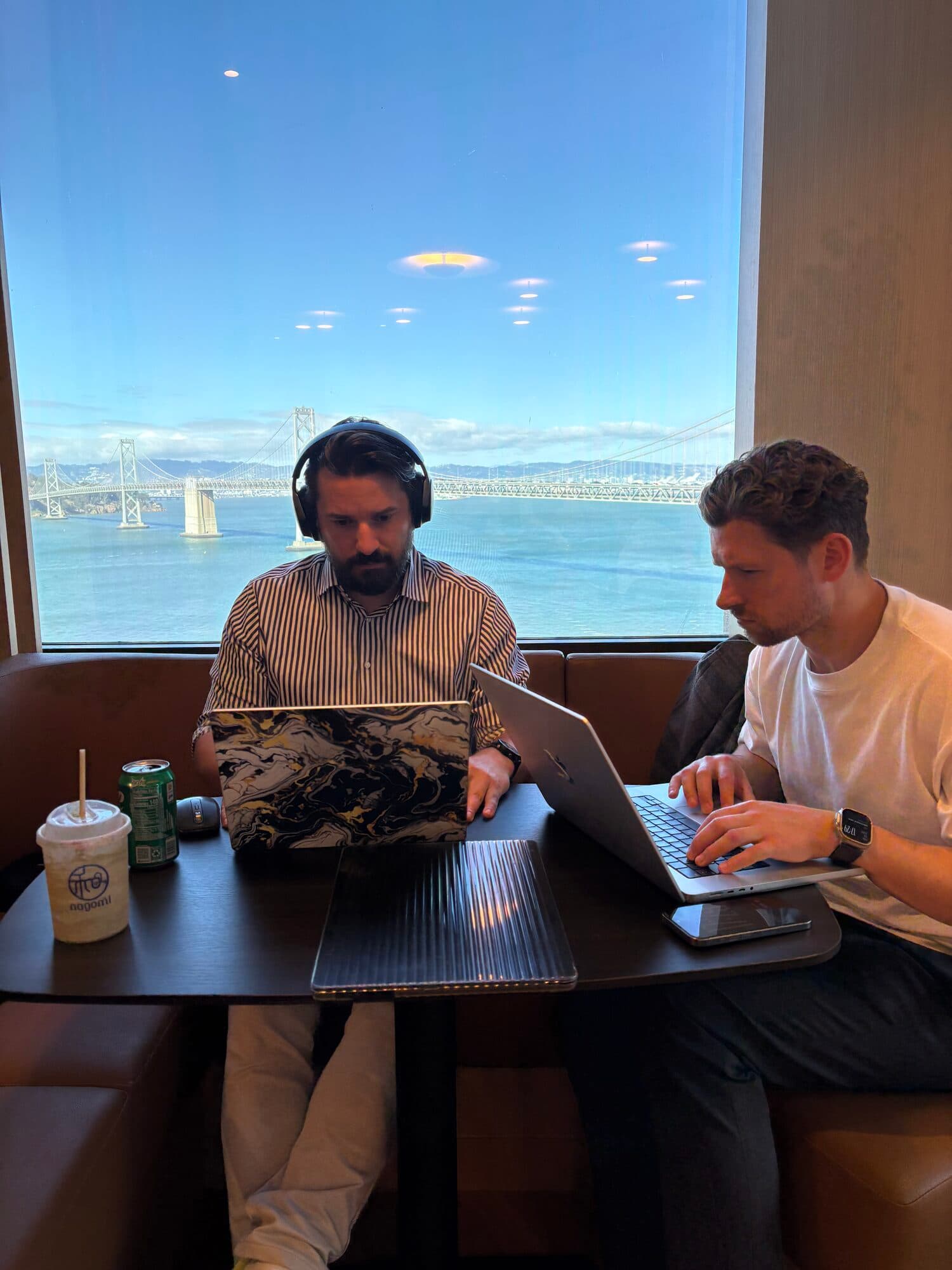 Two builders working on laptops at a window booth above the water during an AI BEAVERS session