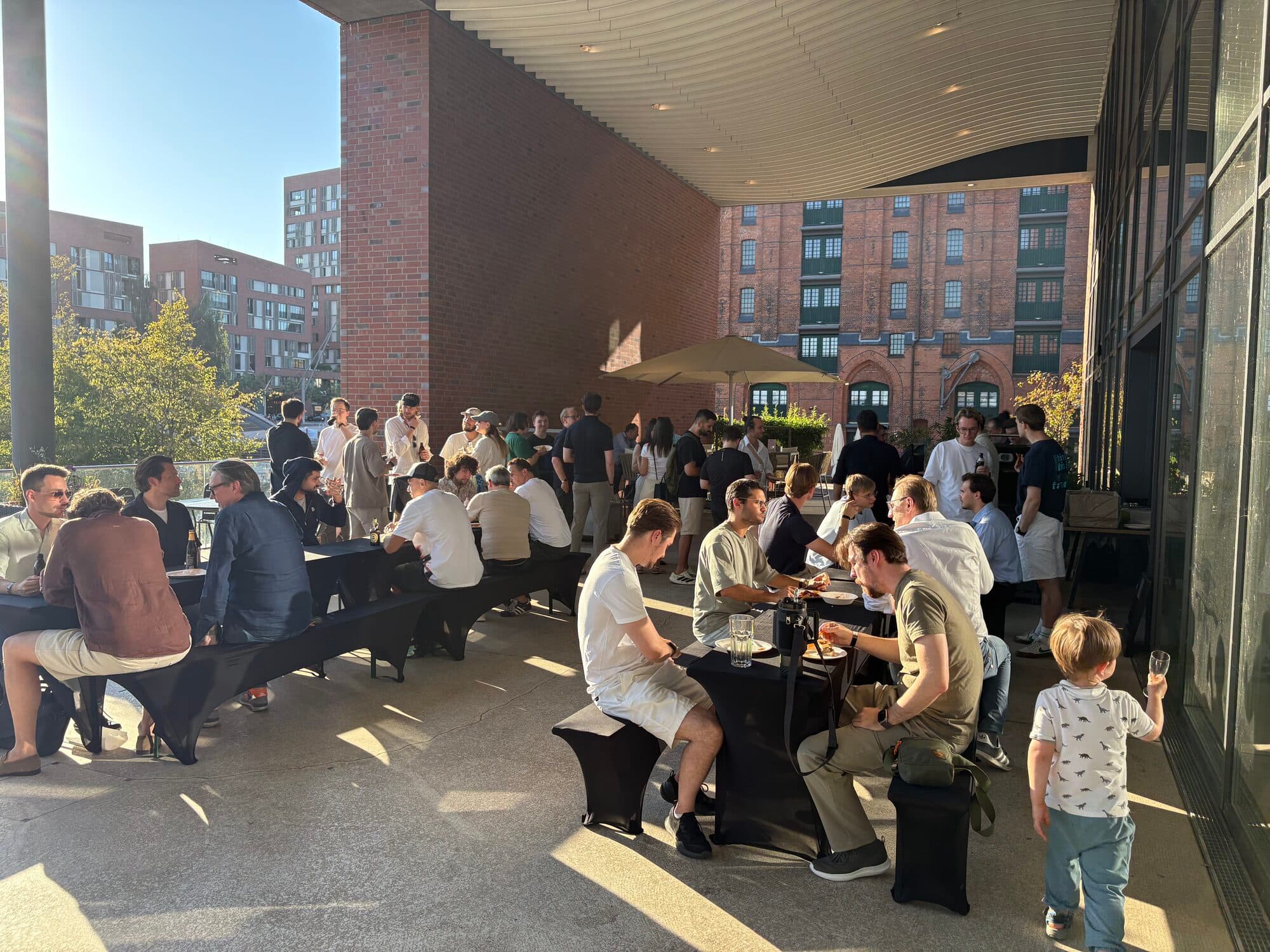 Members sharing tables and conversation in a sunlit courtyard at a local AI BEAVERS event