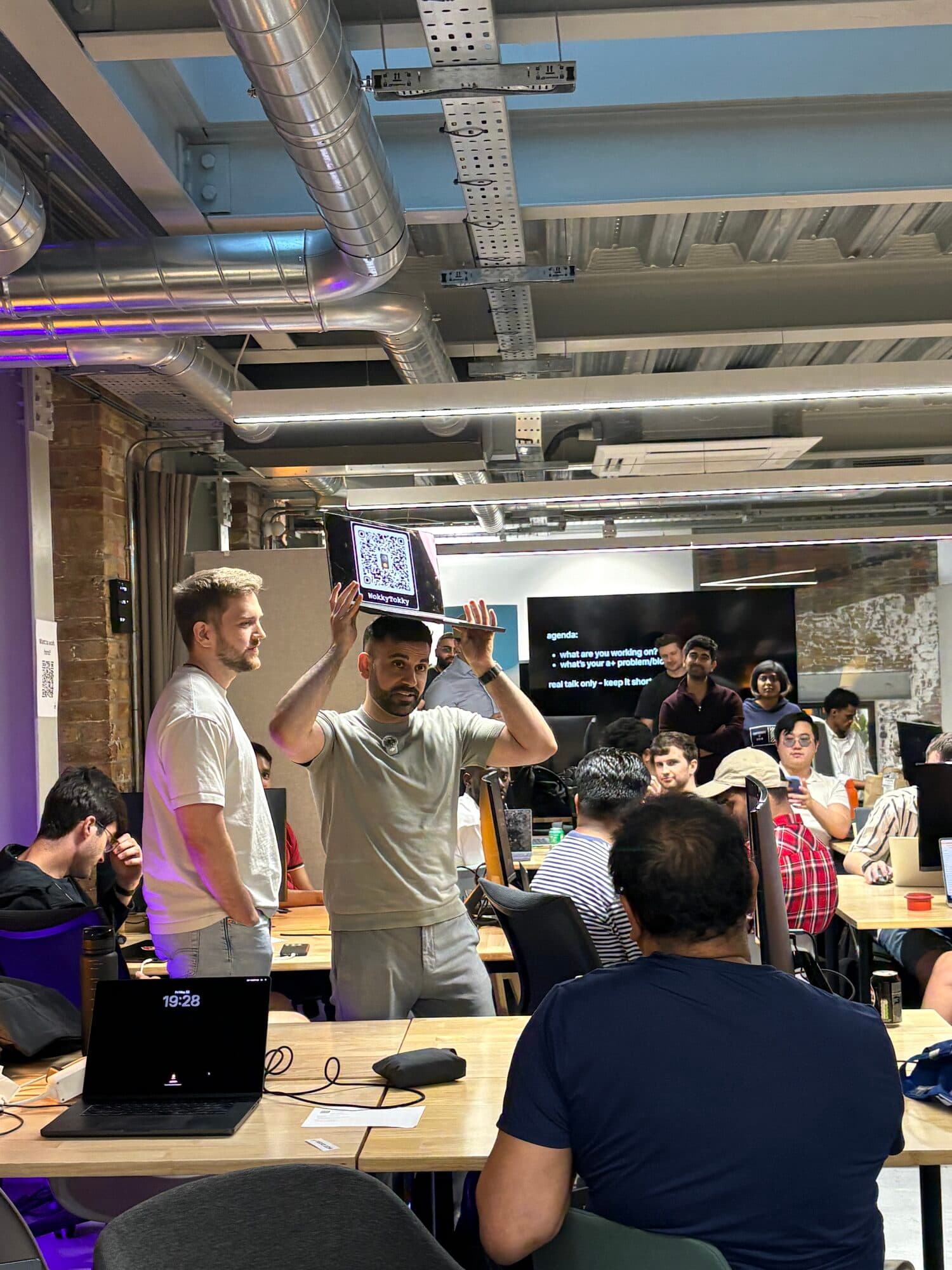 Members at laptop-covered tables while two attendees talk in the foreground at an AI BEAVERS event