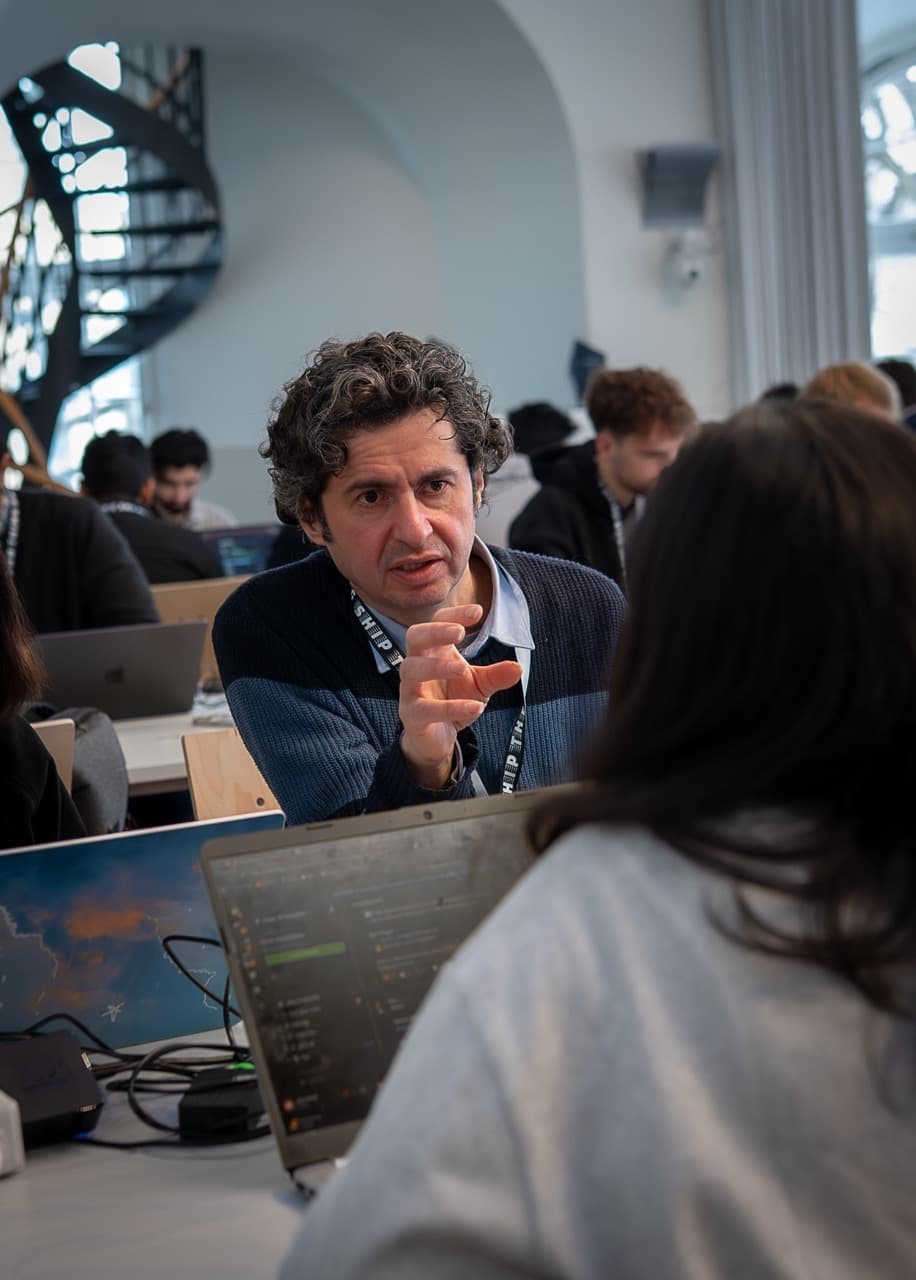 A builder explaining an idea across a table of laptops at the AI BEAVERS January 2026 hackathon in Hamburg