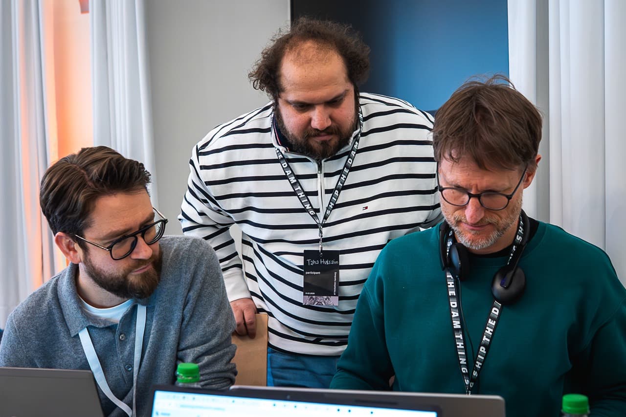 Three teammates gathered around one laptop at the AI BEAVERS January 2026 hackathon in Hamburg