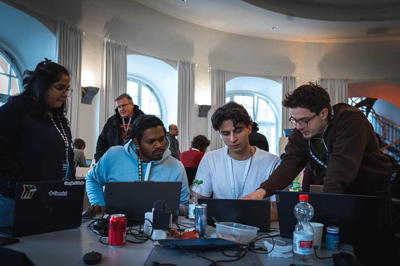 Teams working at long tables by tall windows during the AI BEAVERS January 2026 hackathon in Hamburg