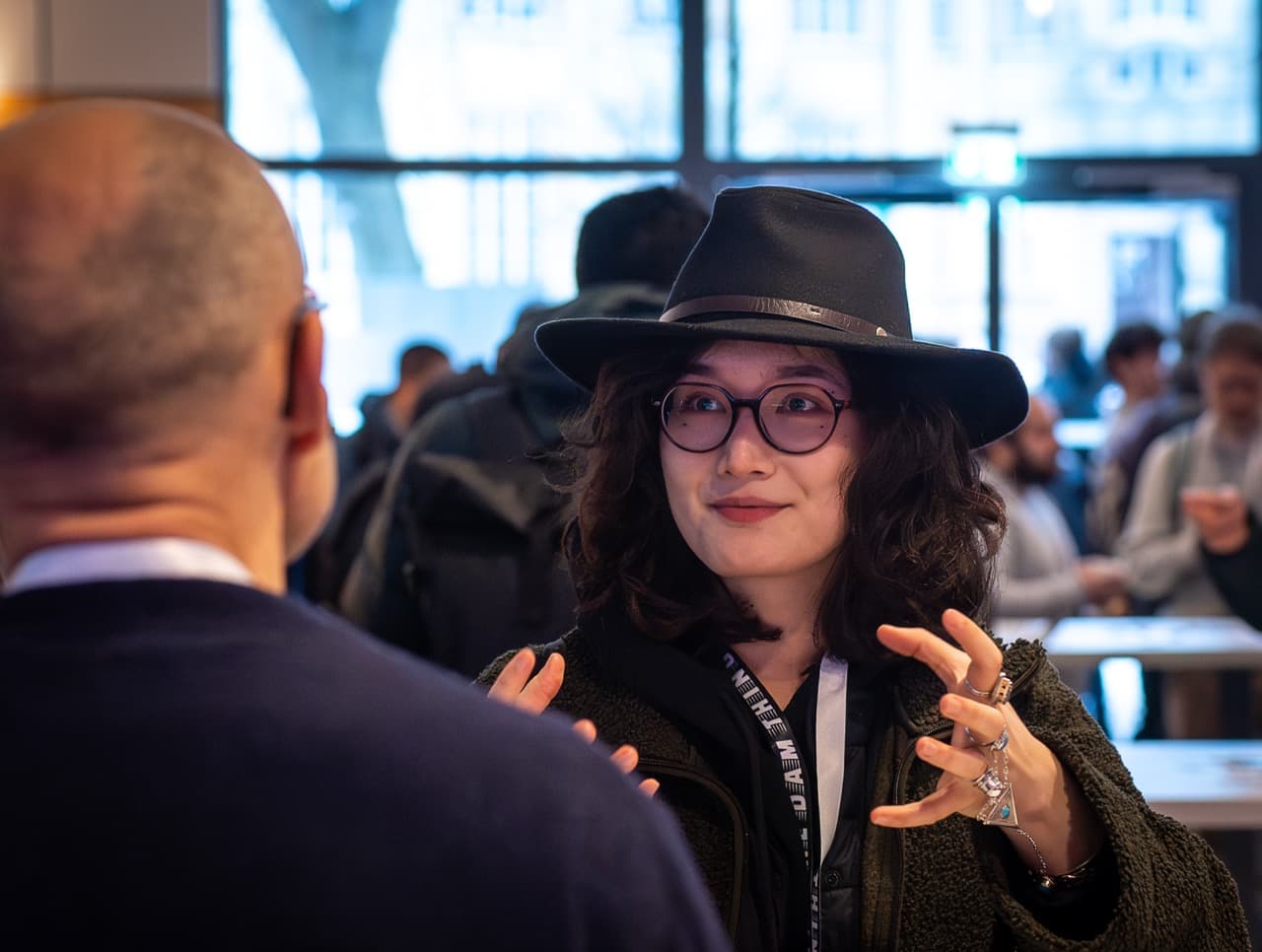 An attendee in a black hat and glasses talking with her hands at the AI BEAVERS January 2026 hackathon in Hamburg